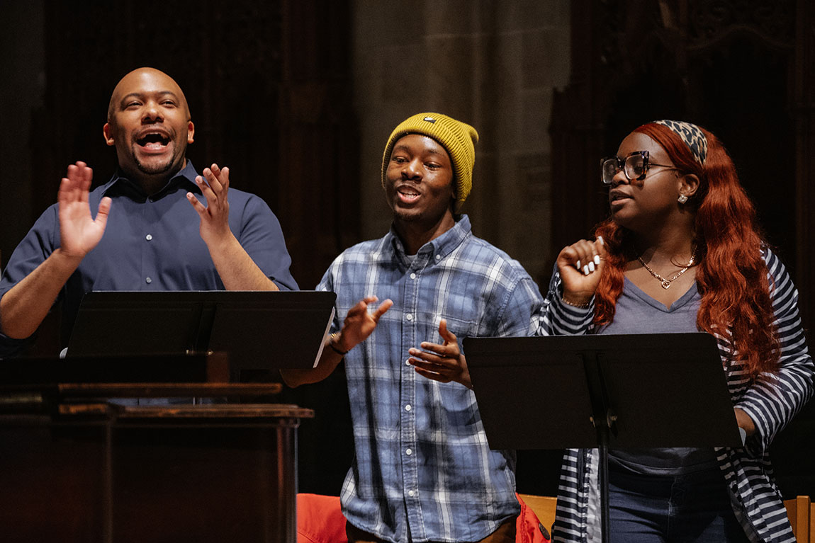 Three young Black people sing and clap their hands during a Gospel music performance